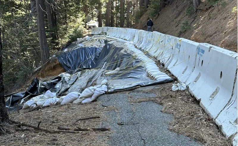The failed section of the Skyway: the embankment covered in plastic sheeting and sandbags, with concrete K-rail barriers separating it from the remaining strip of pavement